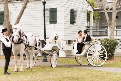 A bride and groom sit in a horse and carriage in front of the Barkley House wedding venue
