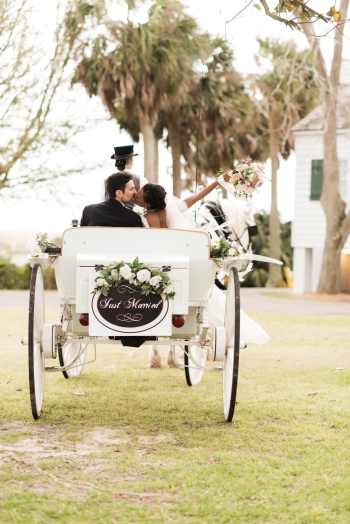 A bride and groom kiss in a white horse drawn carriage