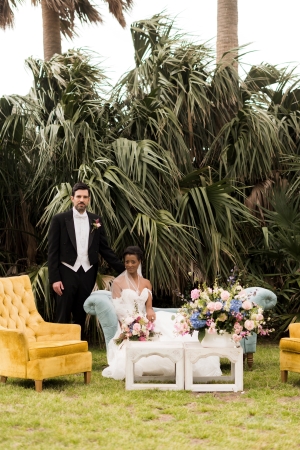 Posed photo of a bride and groom on a couch in front of lush palm trees outside of Barkley House wedding venue