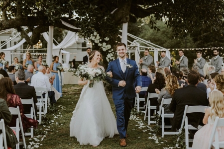 A bride and groom exit a lavishly decorated ceremony on the Barkley House lawn